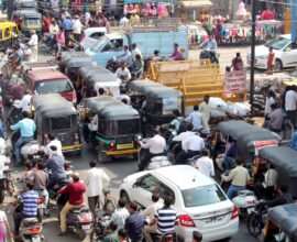 Crowded urban street with cars, bikes, and auto rickshaws in bustling city traffic.