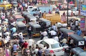 Crowded urban street with cars, bikes, and auto rickshaws in bustling city traffic.