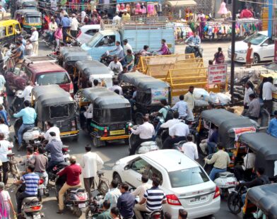 Crowded urban street with cars, bikes, and auto rickshaws in bustling city traffic.
