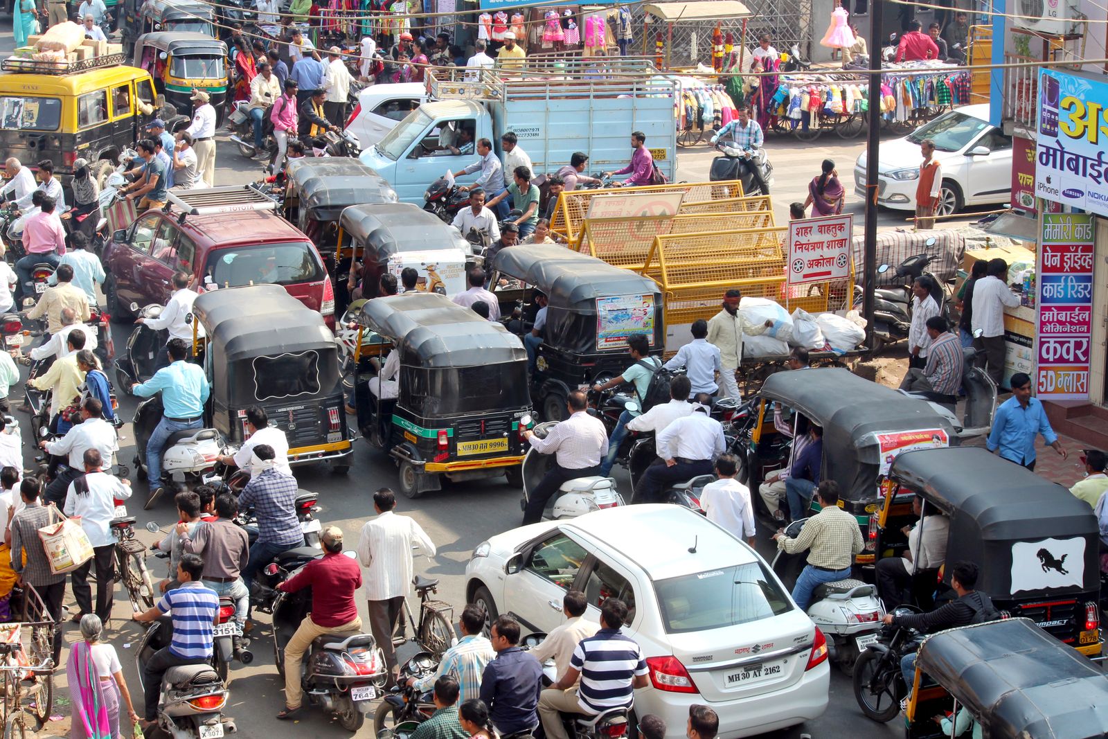 Crowded urban street with cars, bikes, and auto rickshaws in bustling city traffic.
