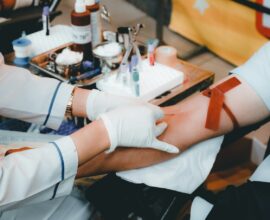A healthcare worker in white gloves drawing blood from a person's arm