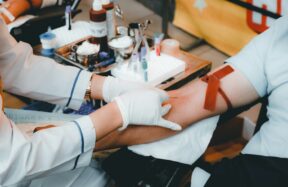 A healthcare worker in white gloves drawing blood from a person's arm
