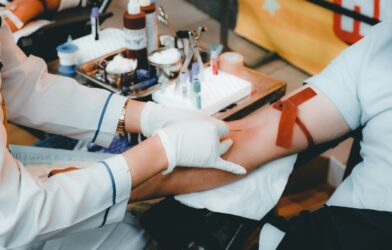 A healthcare worker in white gloves drawing blood from a person's arm