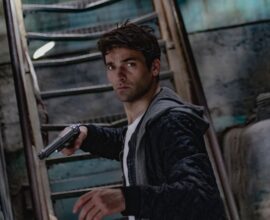 A man holding a gun in a dimly lit, mysterious urban setting.