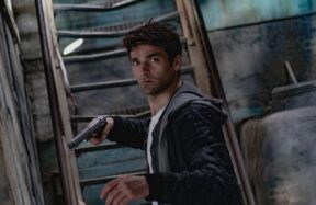 A man holding a gun in a dimly lit, mysterious urban setting.