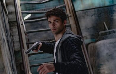 A man holding a gun in a dimly lit, mysterious urban setting.