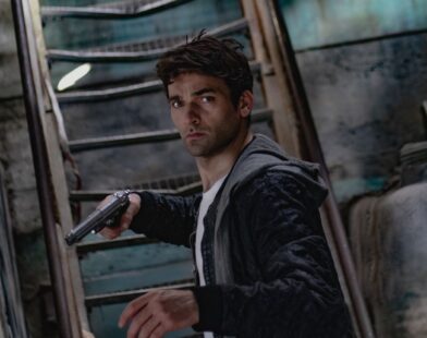 A man holding a gun in a dimly lit, mysterious urban setting.