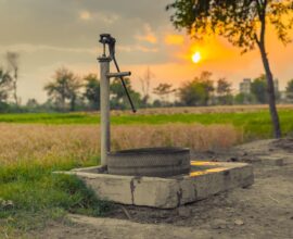 A vintage water pump amidst picturesque fields at sunset, capturing rural tranquility.