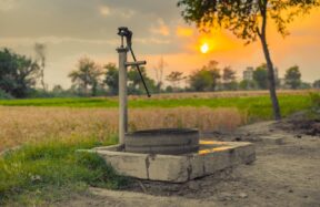 A vintage water pump amidst picturesque fields at sunset, capturing rural tranquility.