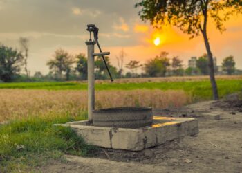 A vintage water pump amidst picturesque fields at sunset, capturing rural tranquility.