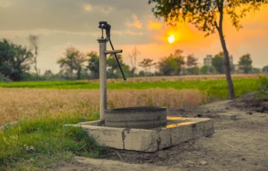 A vintage water pump amidst picturesque fields at sunset, capturing rural tranquility.