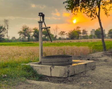 A vintage water pump amidst picturesque fields at sunset, capturing rural tranquility.