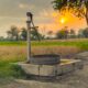 A vintage water pump amidst picturesque fields at sunset, capturing rural tranquility.