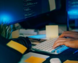 Hands typing on a keyboard with computer screens