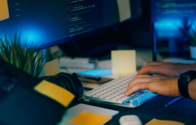 Hands typing on a keyboard with computer screens