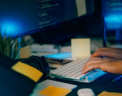 Hands typing on a keyboard with computer screens