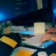 Hands typing on a keyboard with computer screens