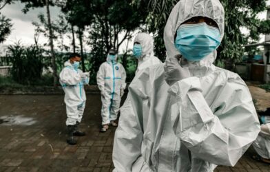 People in white protective suits and blue face masks standing on a paved area