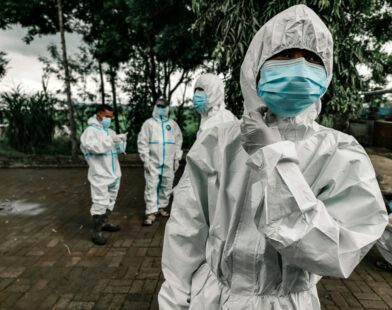 People in white protective suits and blue face masks standing on a paved area