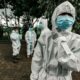 People in white protective suits and blue face masks standing on a paved area