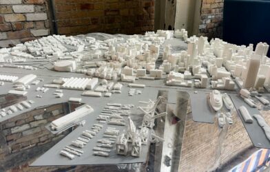 A white architectural model of a city skyline and harbor on a reflective surface