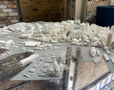 A white architectural model of a city skyline and harbor on a reflective surface