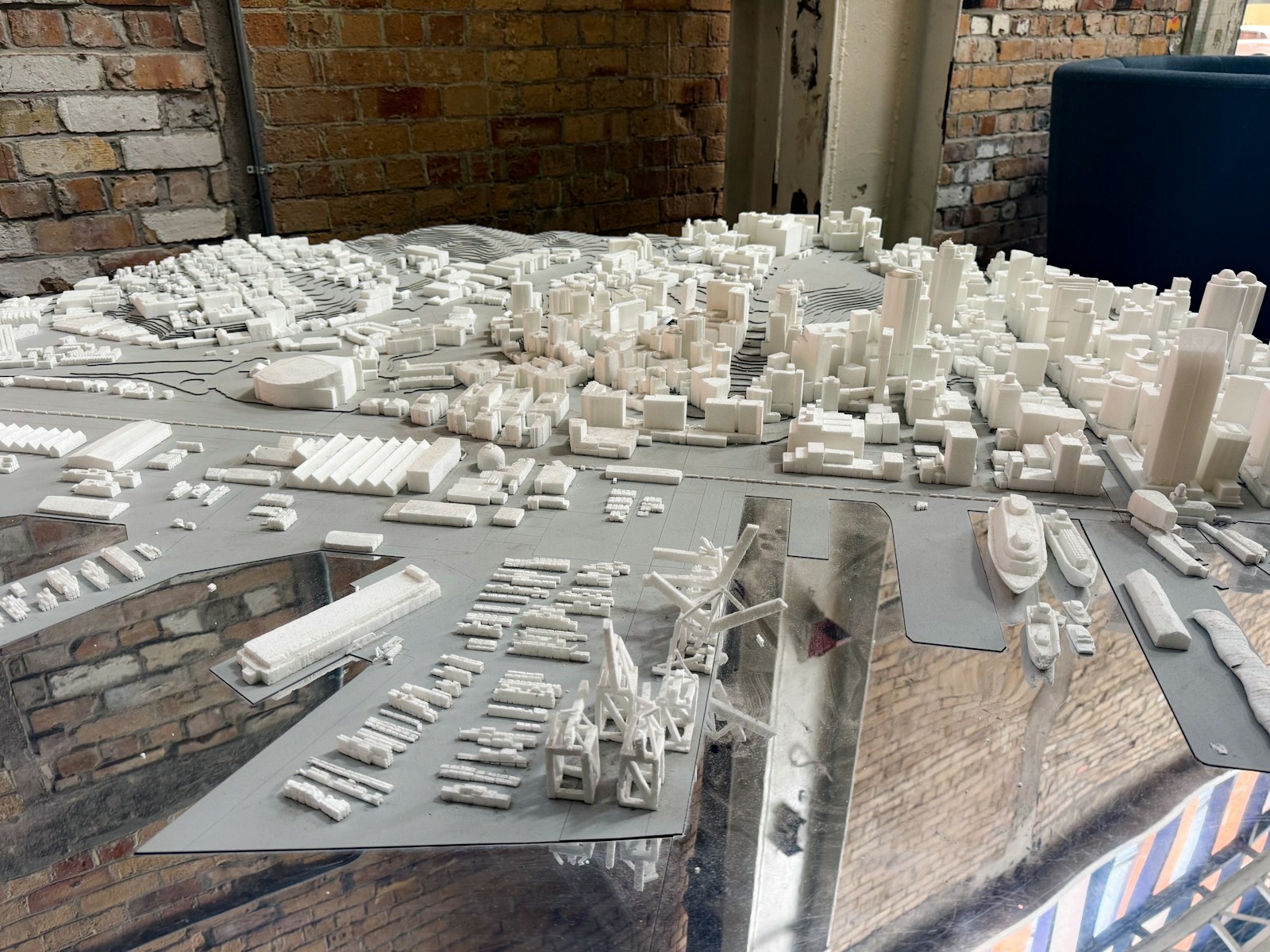 A white architectural model of a city skyline and harbor on a reflective surface