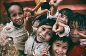 five children smiling while doing peace hand sign