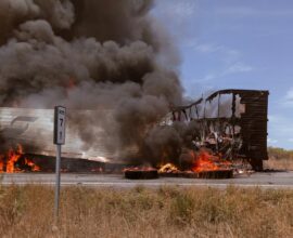 A large truck on fire on the side of the road