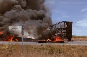 A large truck on fire on the side of the road