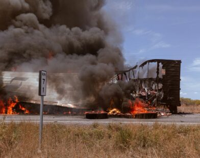 A large truck on fire on the side of the road