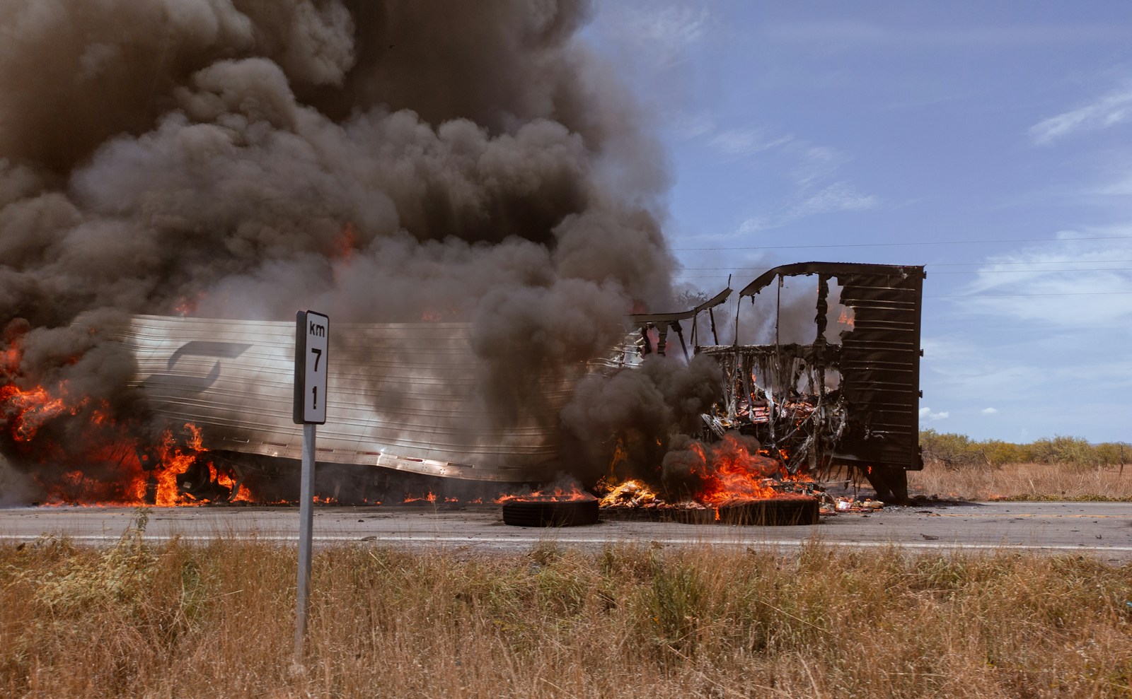 A large truck on fire on the side of the road