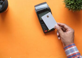 A person holding a blank credit card near a payment terminal on orange