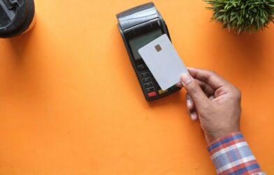 A person holding a blank credit card near a payment terminal on orange