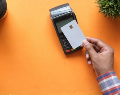 A person holding a blank credit card near a payment terminal on orange