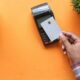 A person holding a blank credit card near a payment terminal on orange
