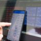 A hand pointing at a smartphone displaying currency quotes against a laptop