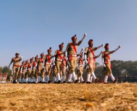 group of people in red and white shirts and pants jumping on brown field during daytime
