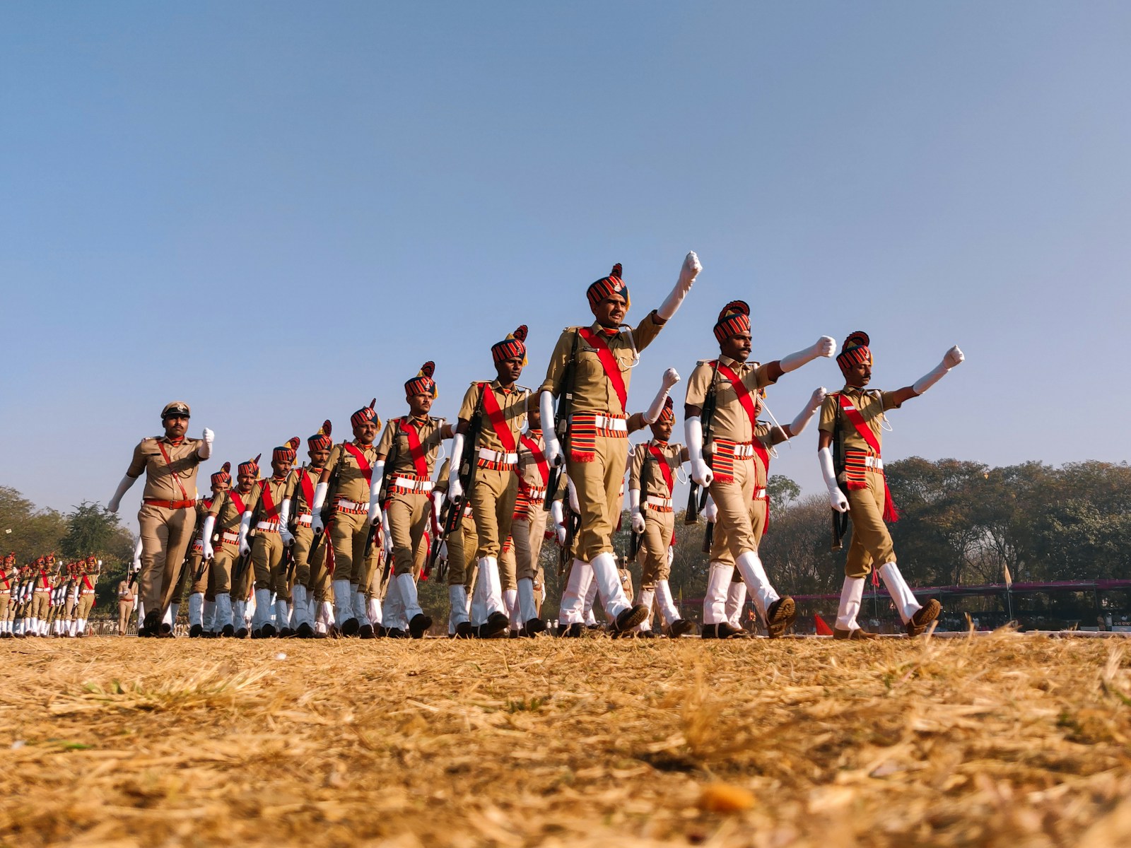 group of people in red and white shirts and pants jumping on brown field during daytime