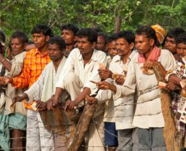 Many men standing outdoors, some holding small objects