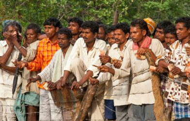 Many men standing outdoors, some holding small objects