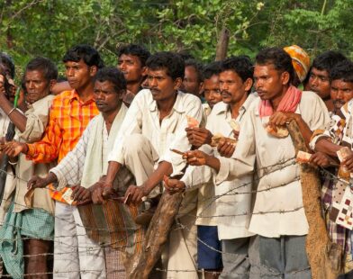 Many men standing outdoors, some holding small objects