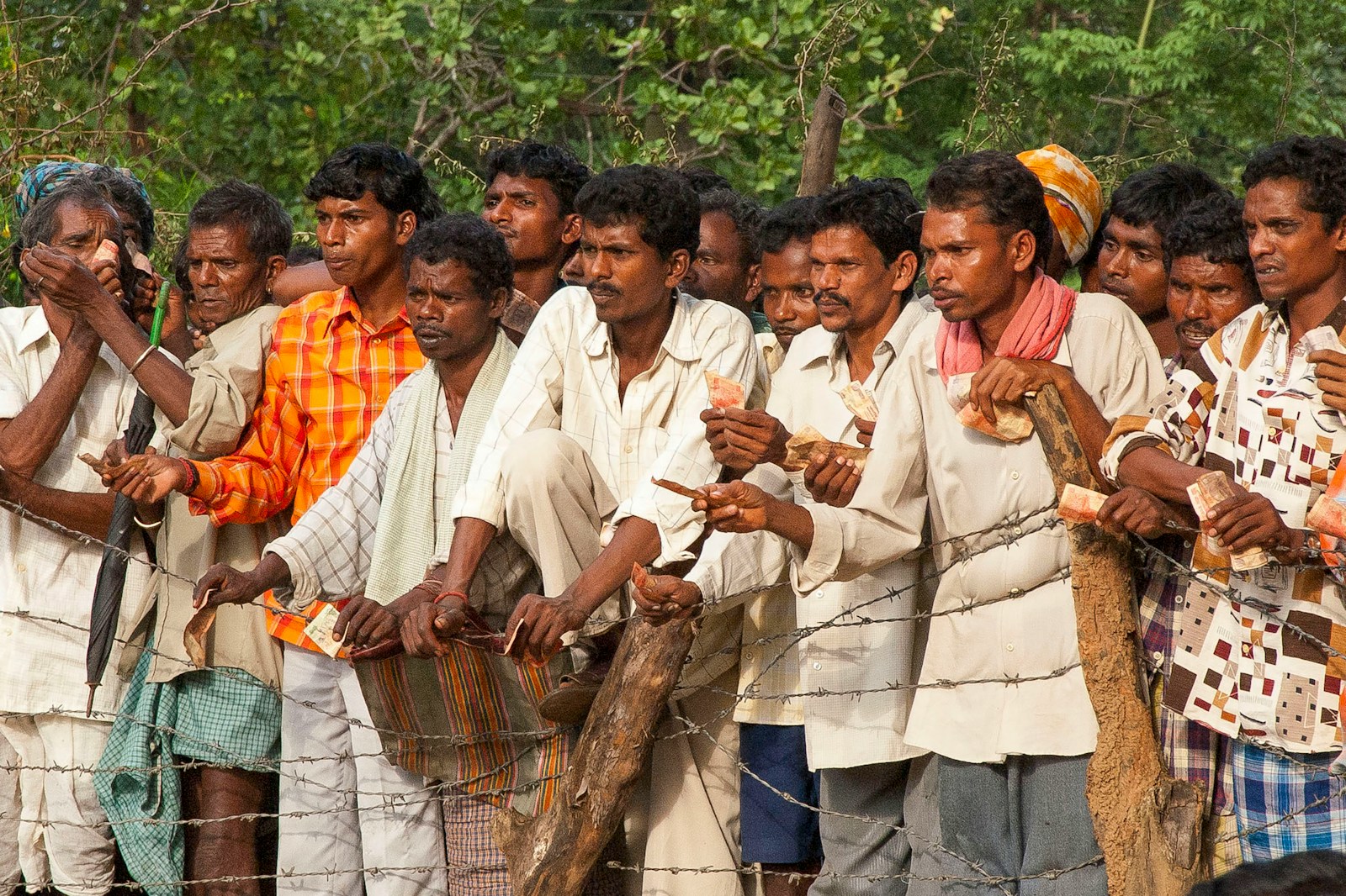 Many men standing outdoors, some holding small objects