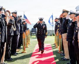 Navy officers salute during a ceremony on a sunny day