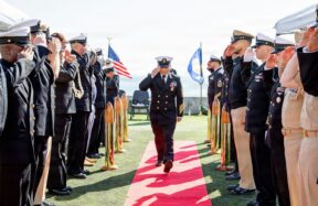 Navy officers salute during a ceremony on a sunny day