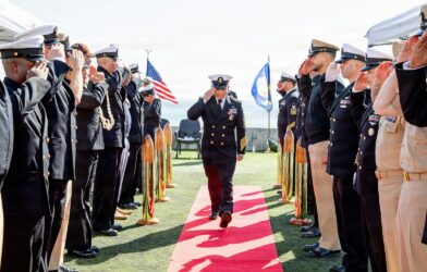 Navy officers salute during a ceremony on a sunny day