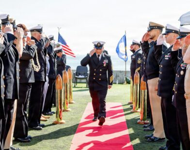 Navy officers salute during a ceremony on a sunny day