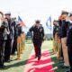 Navy officers salute during a ceremony on a sunny day