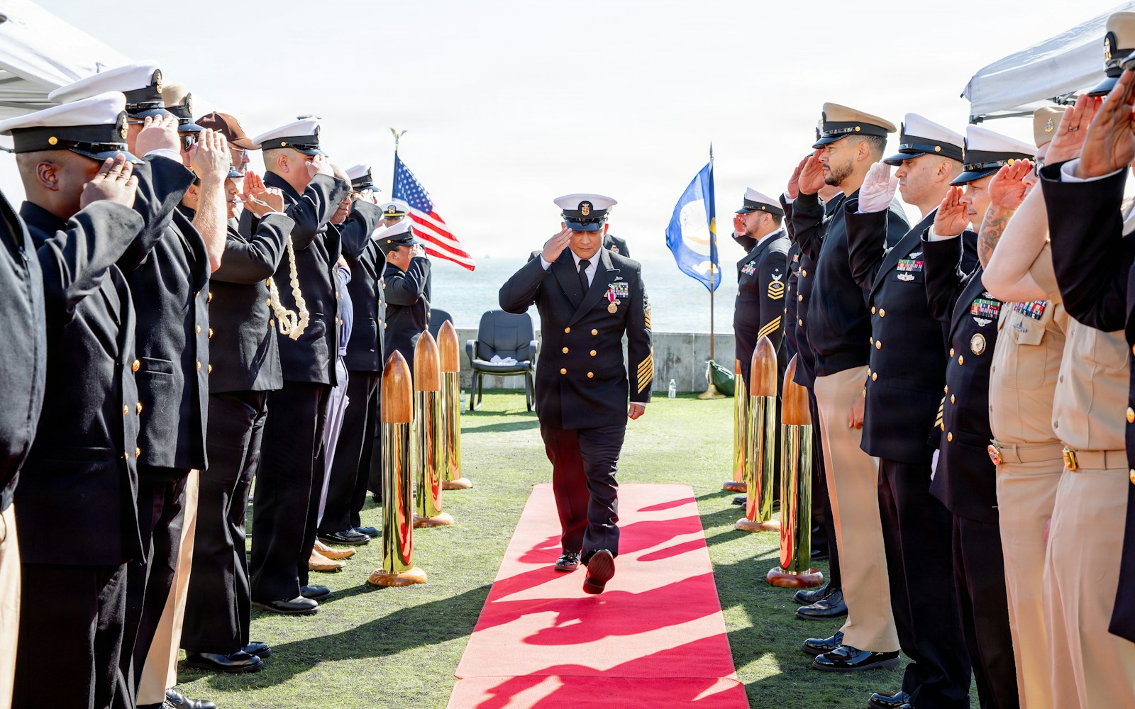 Navy officers salute during a ceremony on a sunny day