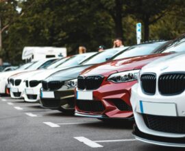 A row of parked cars including white, olive, and red sedans in a lot
